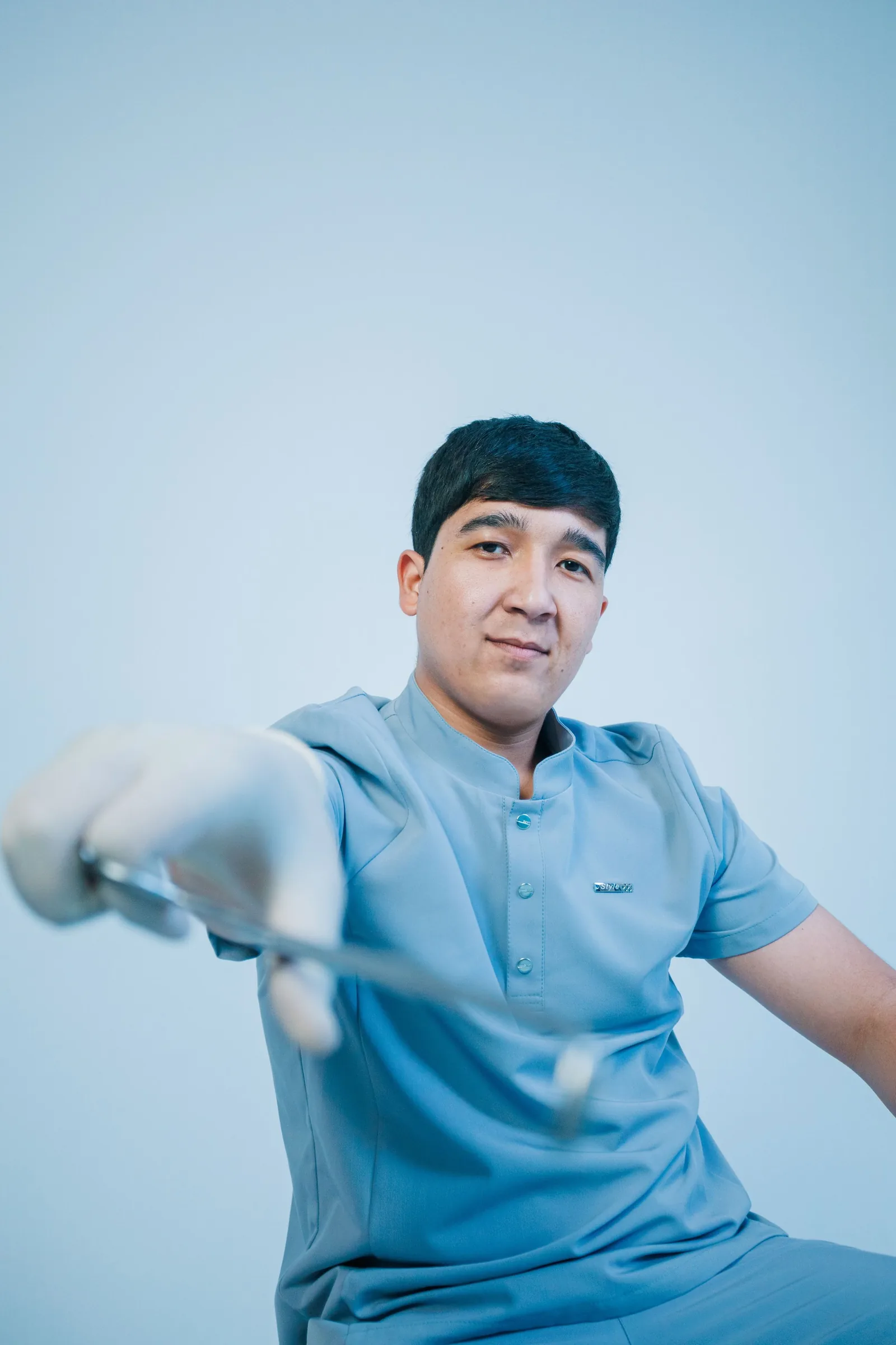 Portrait of a dentist in blue scrubs holding a dental mirror