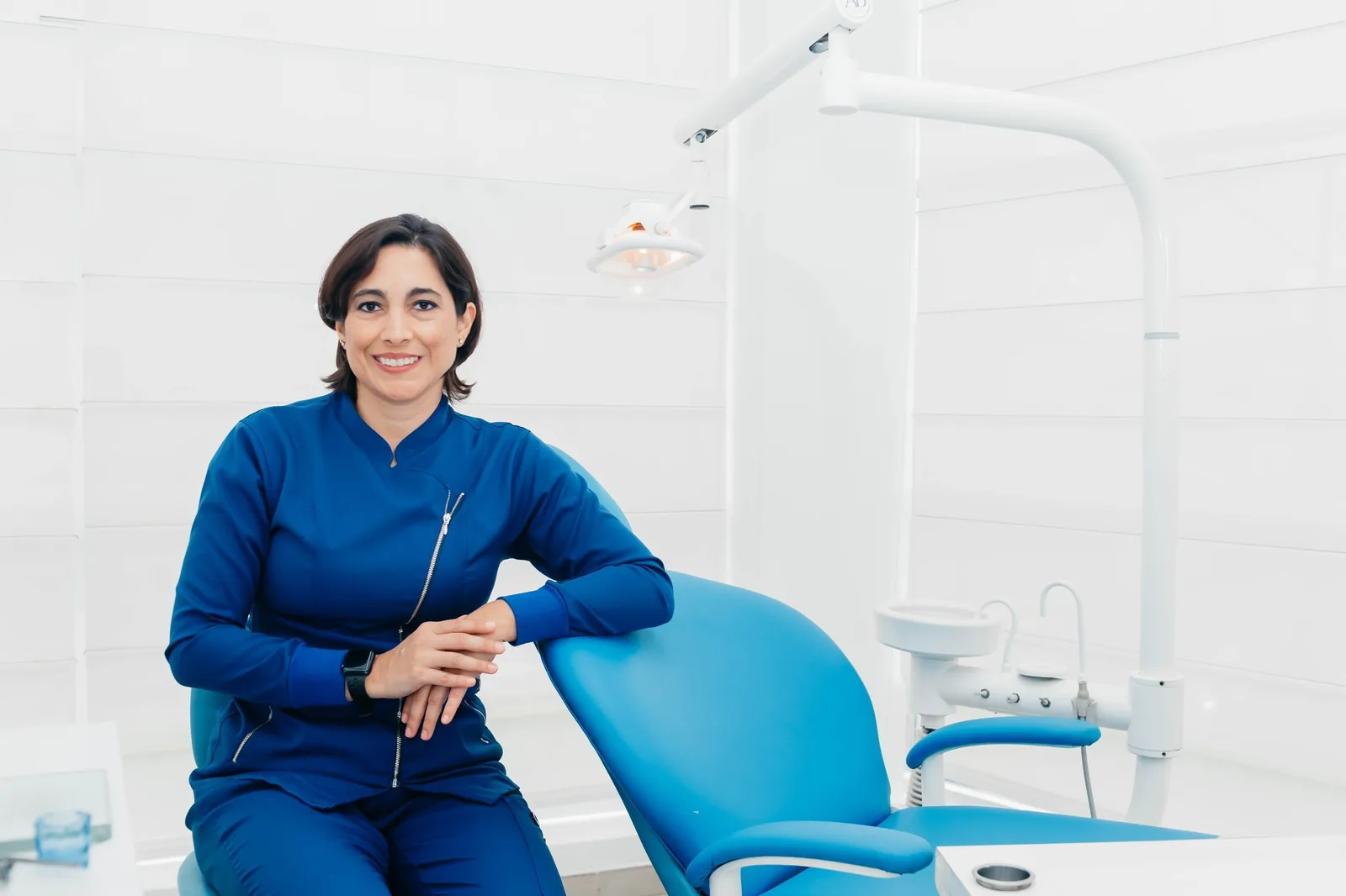 Portrait of a dentist in navy scrubs sitting by a dental chair